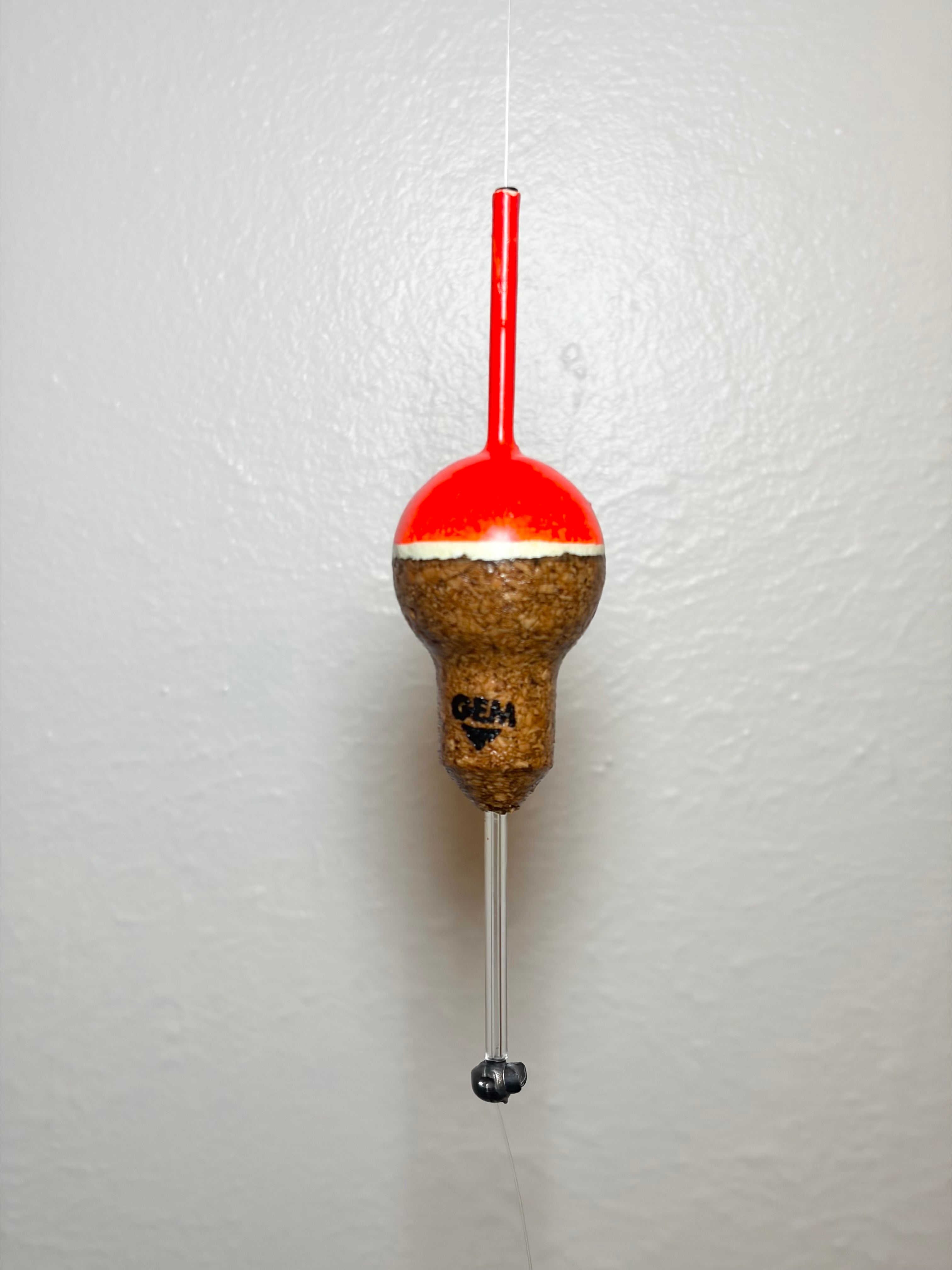 Orange cork fishing slip float attached to a fishing line, on a white background.
