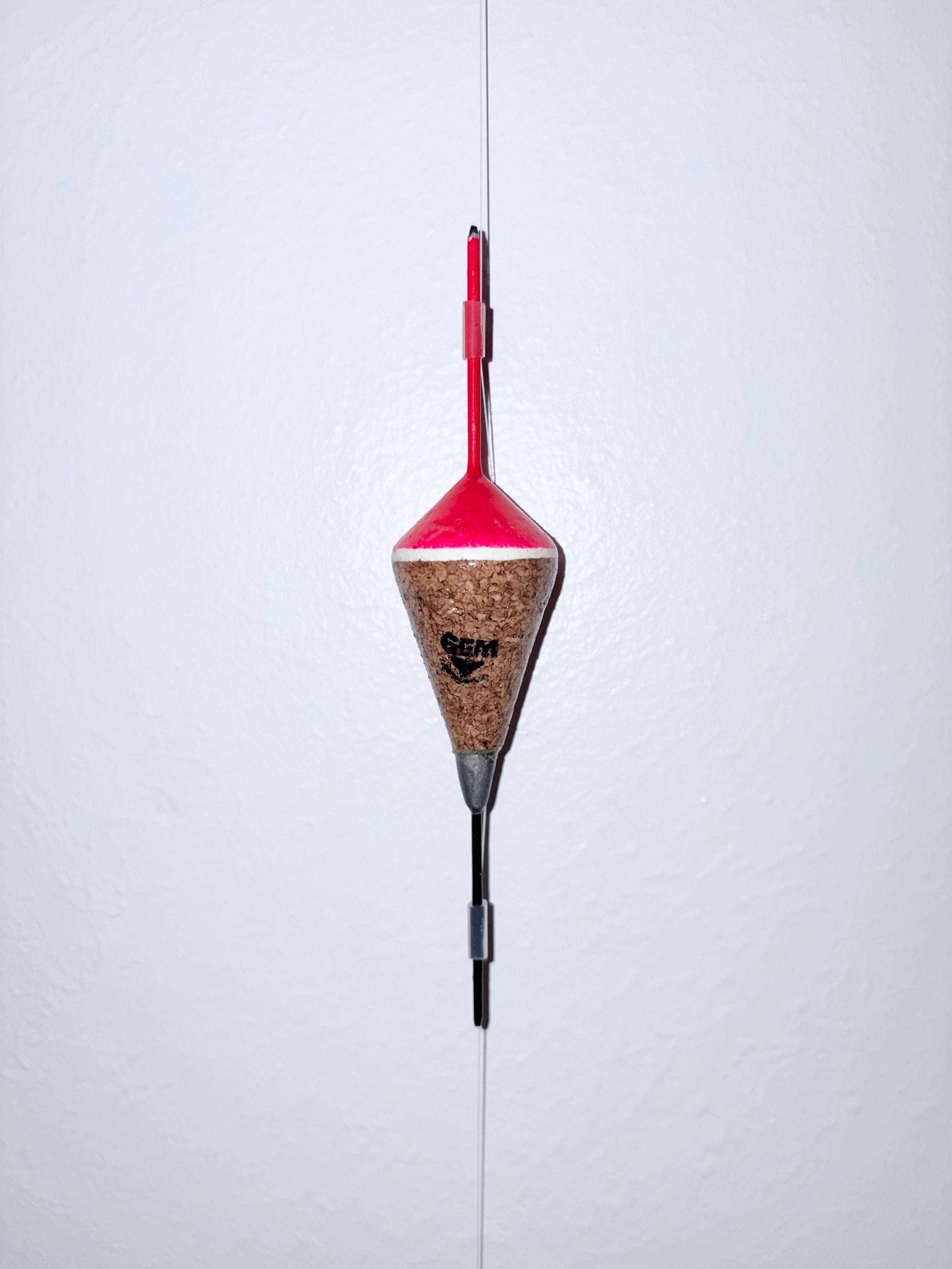 Pink weighted fixed cork fishing float attached to a fishing line, on a white background.