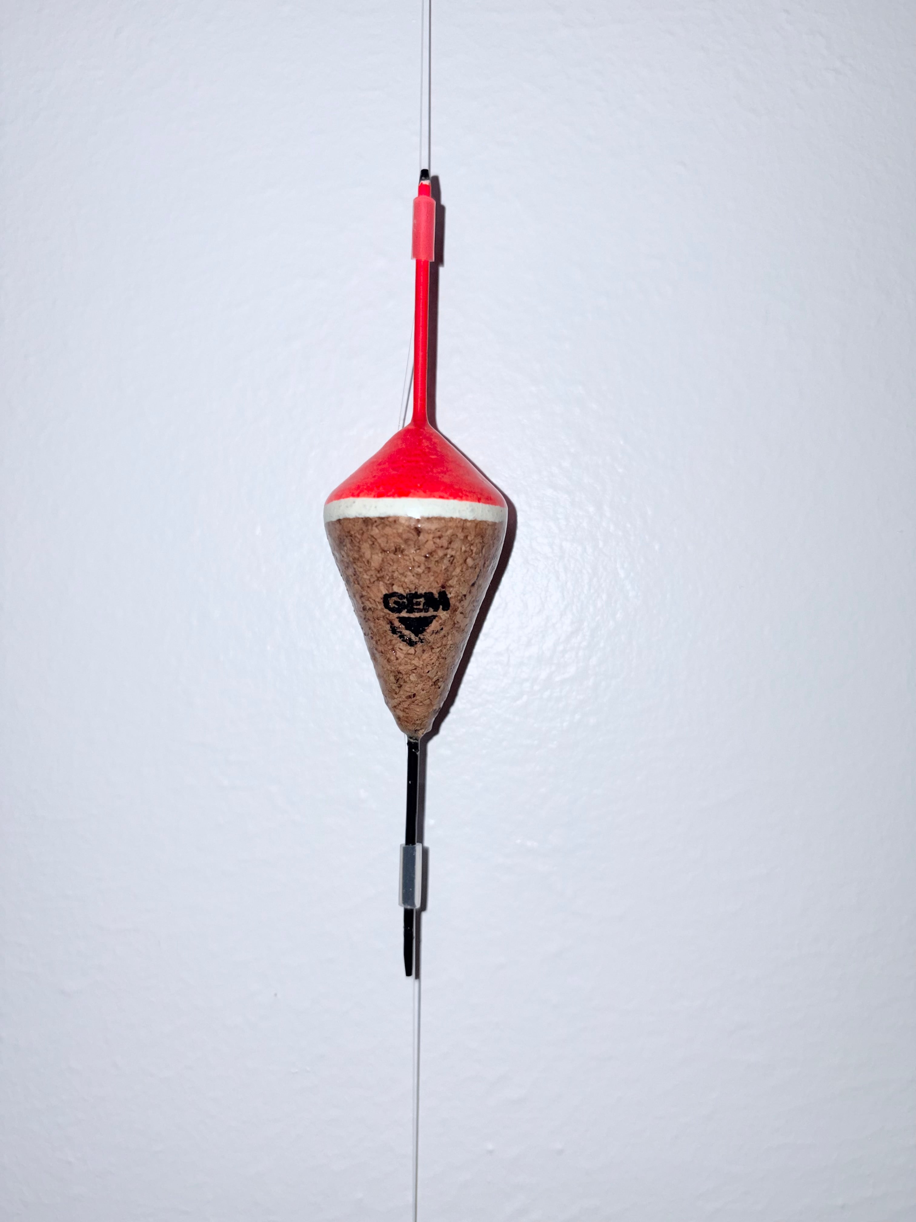 Orange unweighted fixed cork fishing float attached to a fishing line, on a white background.